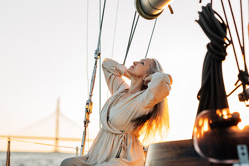 Side view of elegant senior woman sitting on a yacht deck and adjusting her long hair at sunset