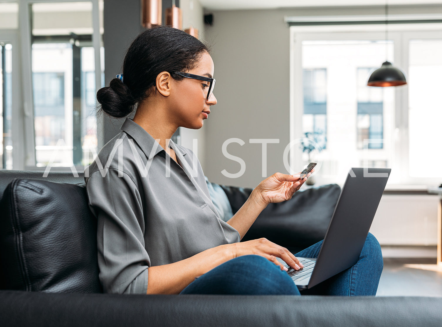 Woman using credit card for paying online, sitting on a sofa in the living room