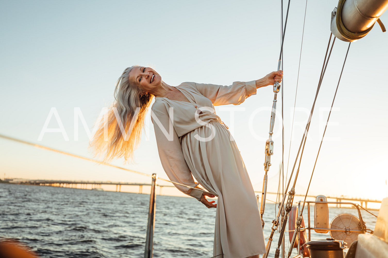 Stylish mature woman holding a rope and enjoying a sunset on a sailboat	