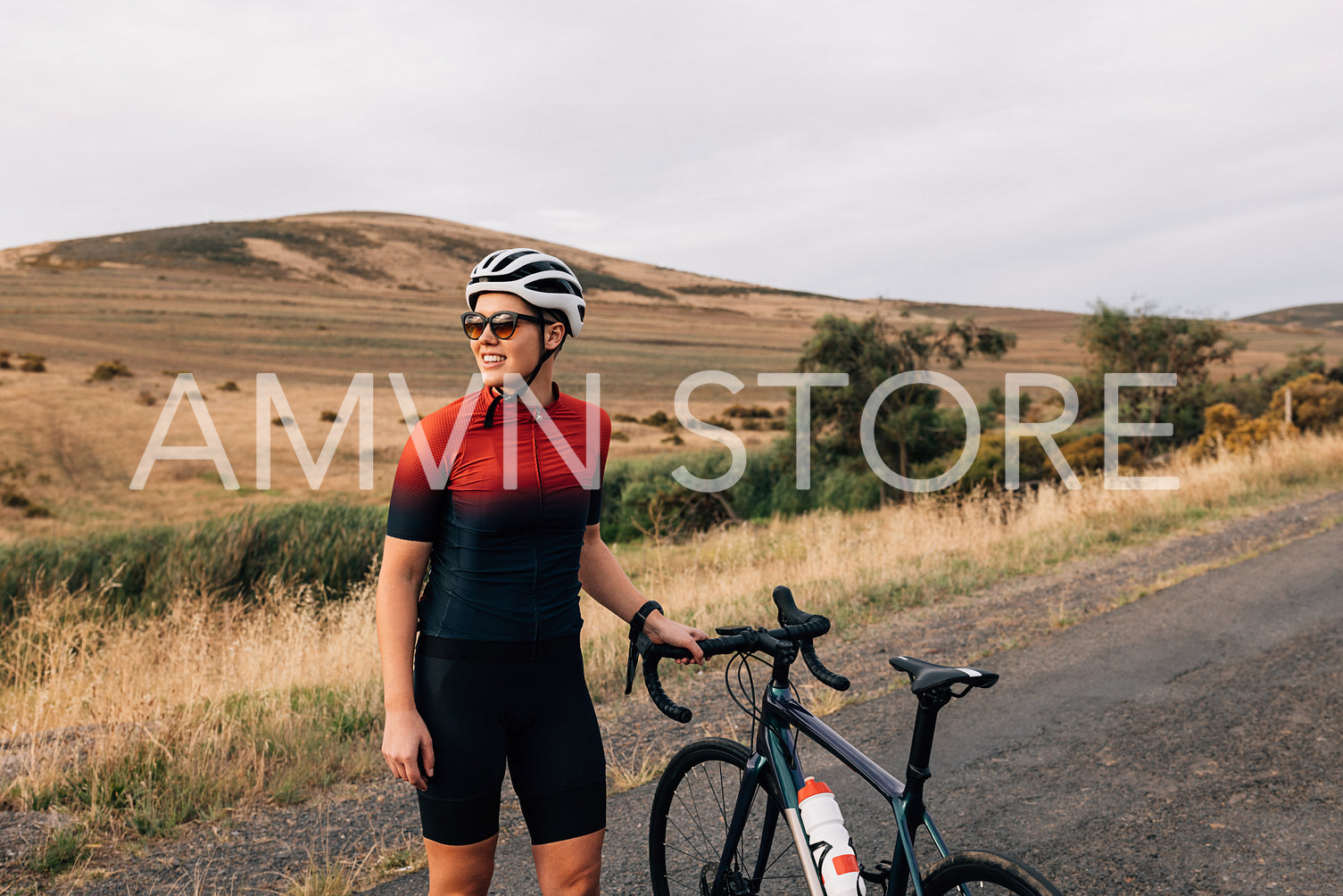 Sportswoman wearing a cycling helmet and sunglasses standing with a bicycle on an empty road