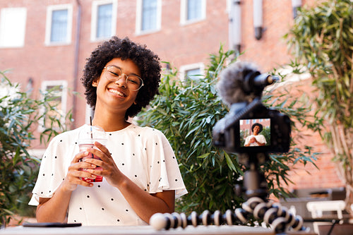 Happy woman recording a video on dslr camera, holding a juice