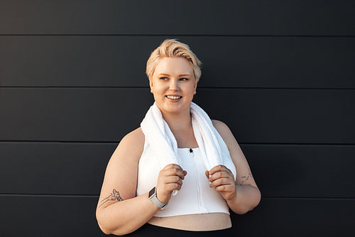 Portrait of a smiling woman in sportswear leaning on wall with a towel around her neck