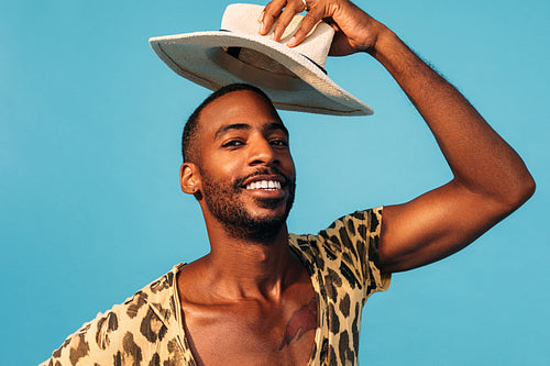 Portrait of a cheerful young man holding hat over his head against a blue background