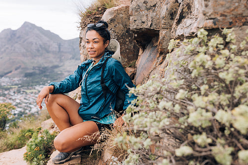 Young woman in sports clothes relaxing during mountain hike looking way, leaning rock