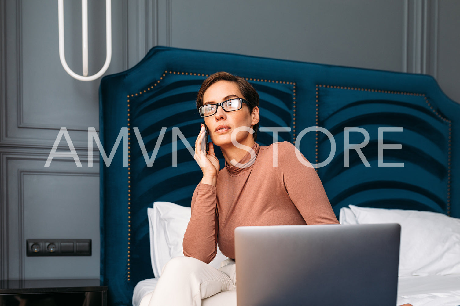 Caucasian woman in casual clothes sitting on bed in hotel room using smartphone and looking at window. Businesswoman working from hotel room.	