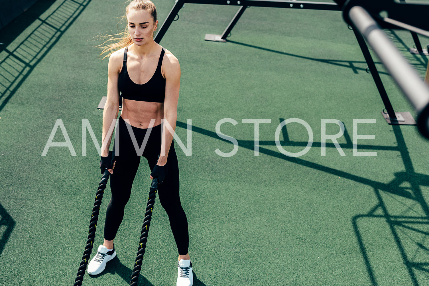 Woman in fitness wear relaxing after workout. Young female with a battle rope in her hands.	
