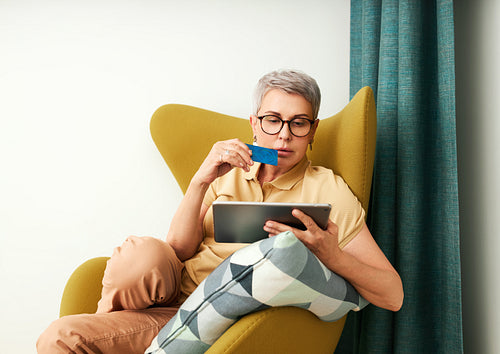 Mature woman in casuals paying by credit card while online shopping from home