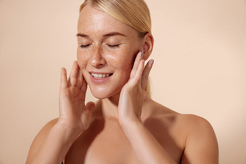 Young smiling woman massaging her face with fingers standing in