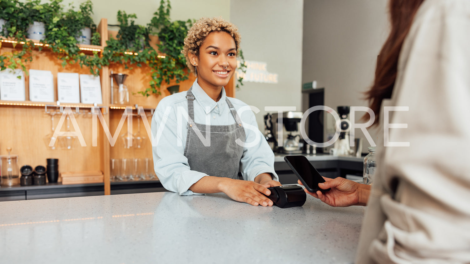 Smiling barista in apron receiving payment from a client in a coffee shop at the counter