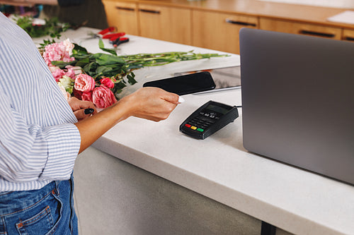 Hand of a woman with smartphone making contactless payment at flower shop.