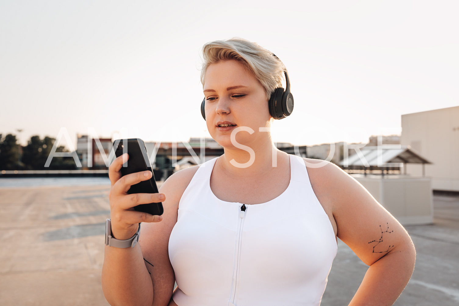 Oversize woman in sports clothes holding a smartphone while standing on the roof at sunset	