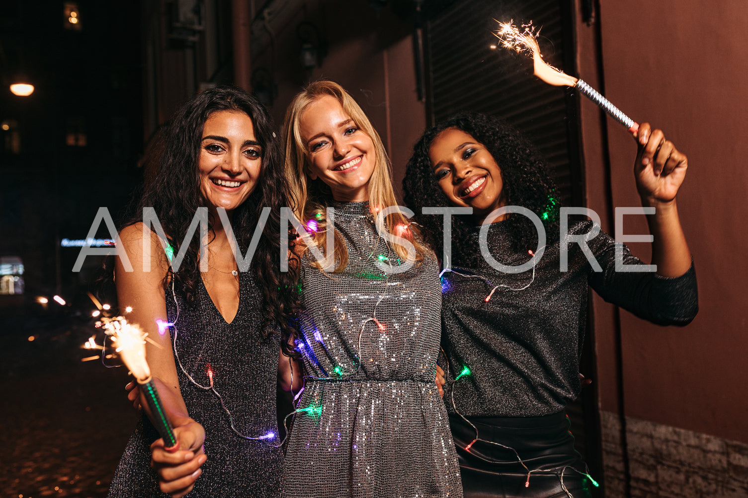 Three women celebrating new year at night with sparklers and christmas lights	