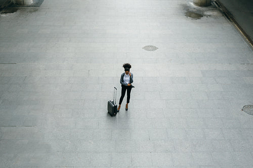 High angle view of young businesswoman standing at airport terminal with a suitcase and talking on mobile phone.