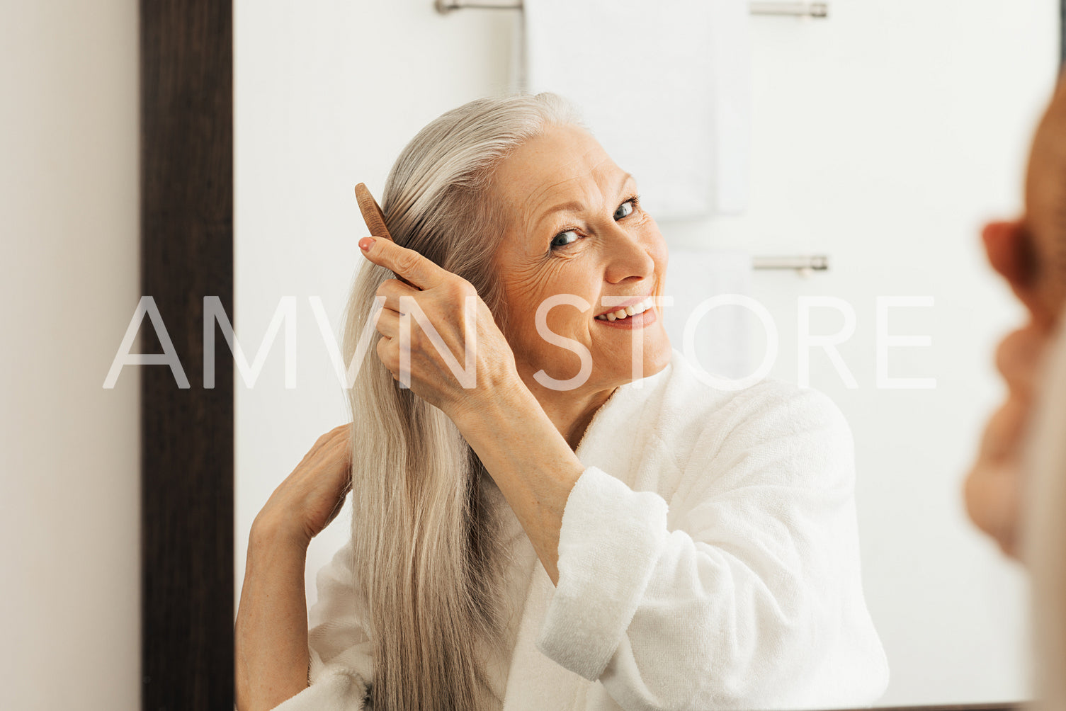 Cheerful senior woman combing her hair looking at a mirror in bathroom