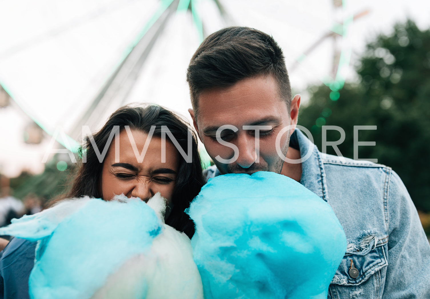 Close-up of a young couple biting blue cotton candy in an amusement park