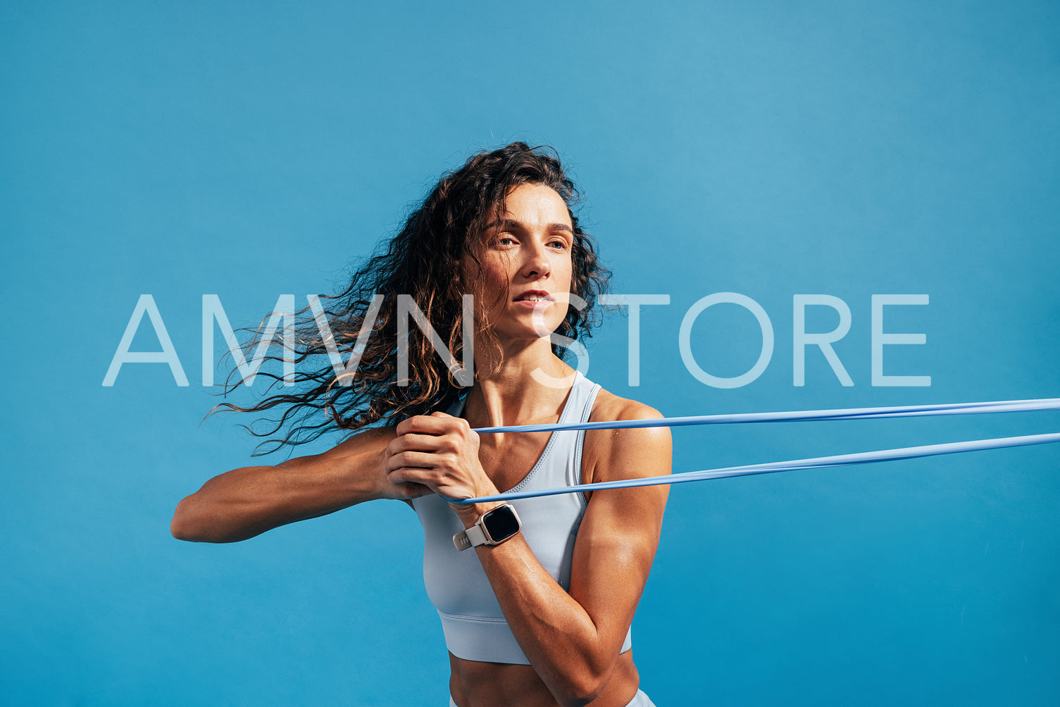 Close up of caucasian woman exercising with a resistance band. Young fitness female training on blue background.