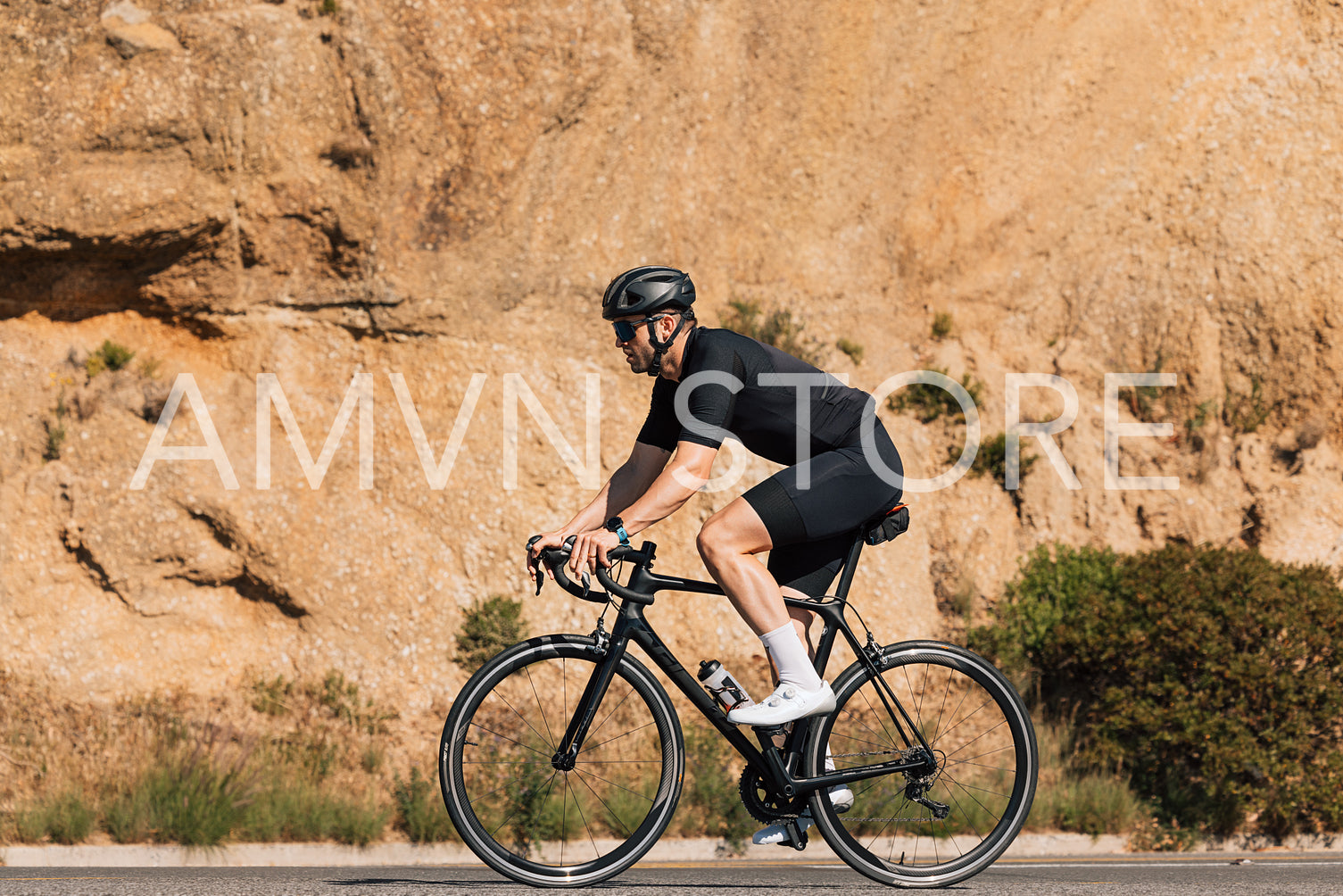 Side view of a cyclist in black sportswear riding his road bicycle