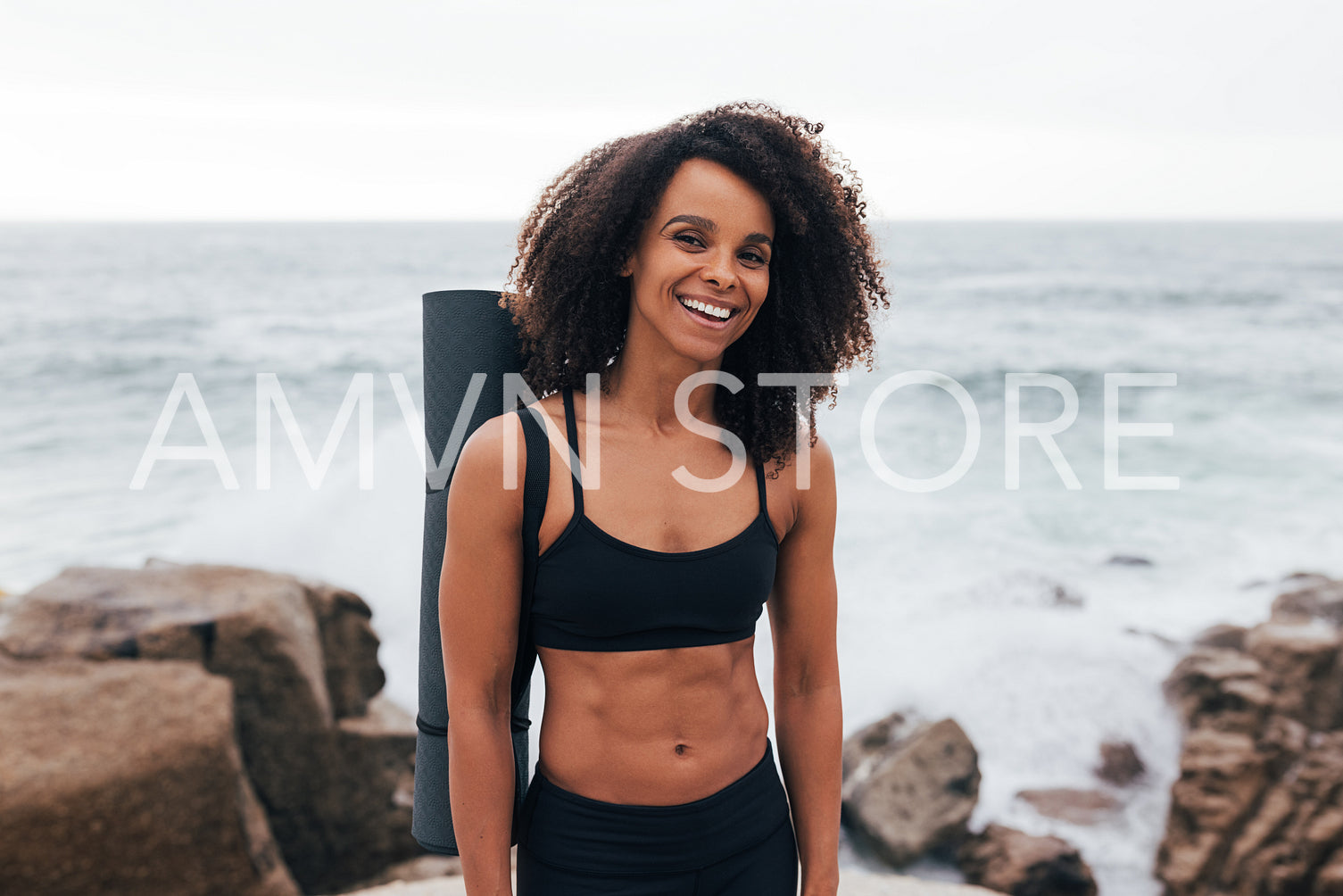 Portrait of a laughing woman with curly hair wearing fitness clothes with yoga mat