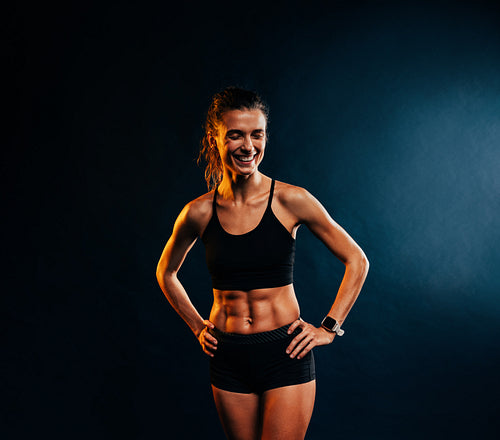 Portrait of young cheerful muscular woman in sportswear posing against black background