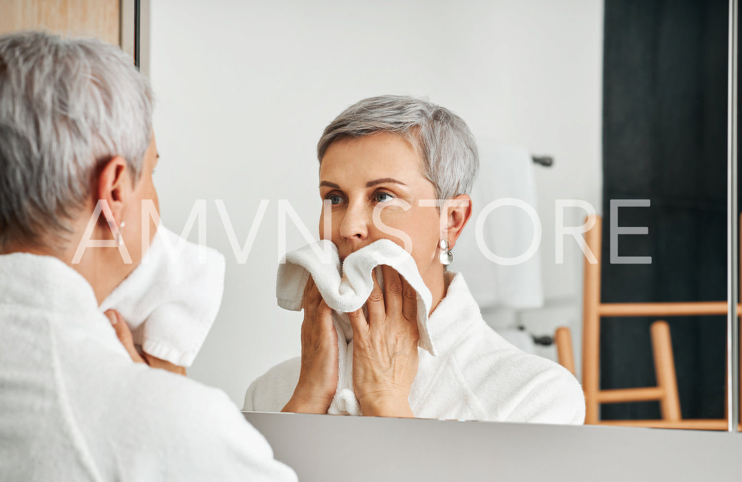 Mature adult woman wiping her face after morning routine in the bathroom	