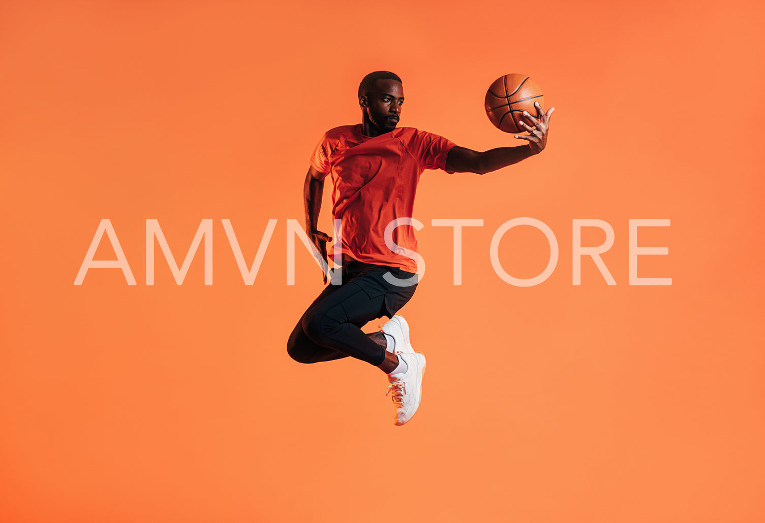 Young man in sportswear practicing basketball against an orange background. African male athlete jumping in the air with basket ball in studio. 