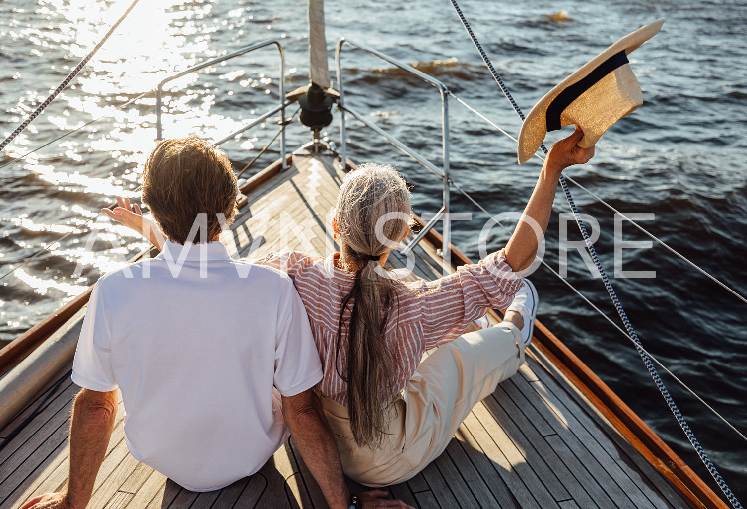 Back view of a happy mature woman waving her straw hat on a yacht. Senior couple enjoying a vacation on a sail boat.	