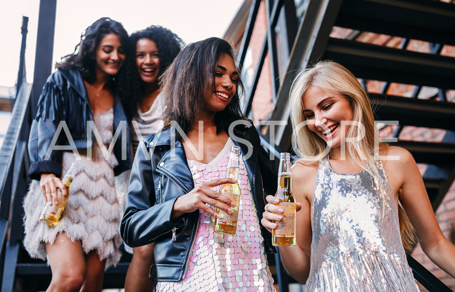 Group of young woman holds bottles of beer while stepping down on the stairs	