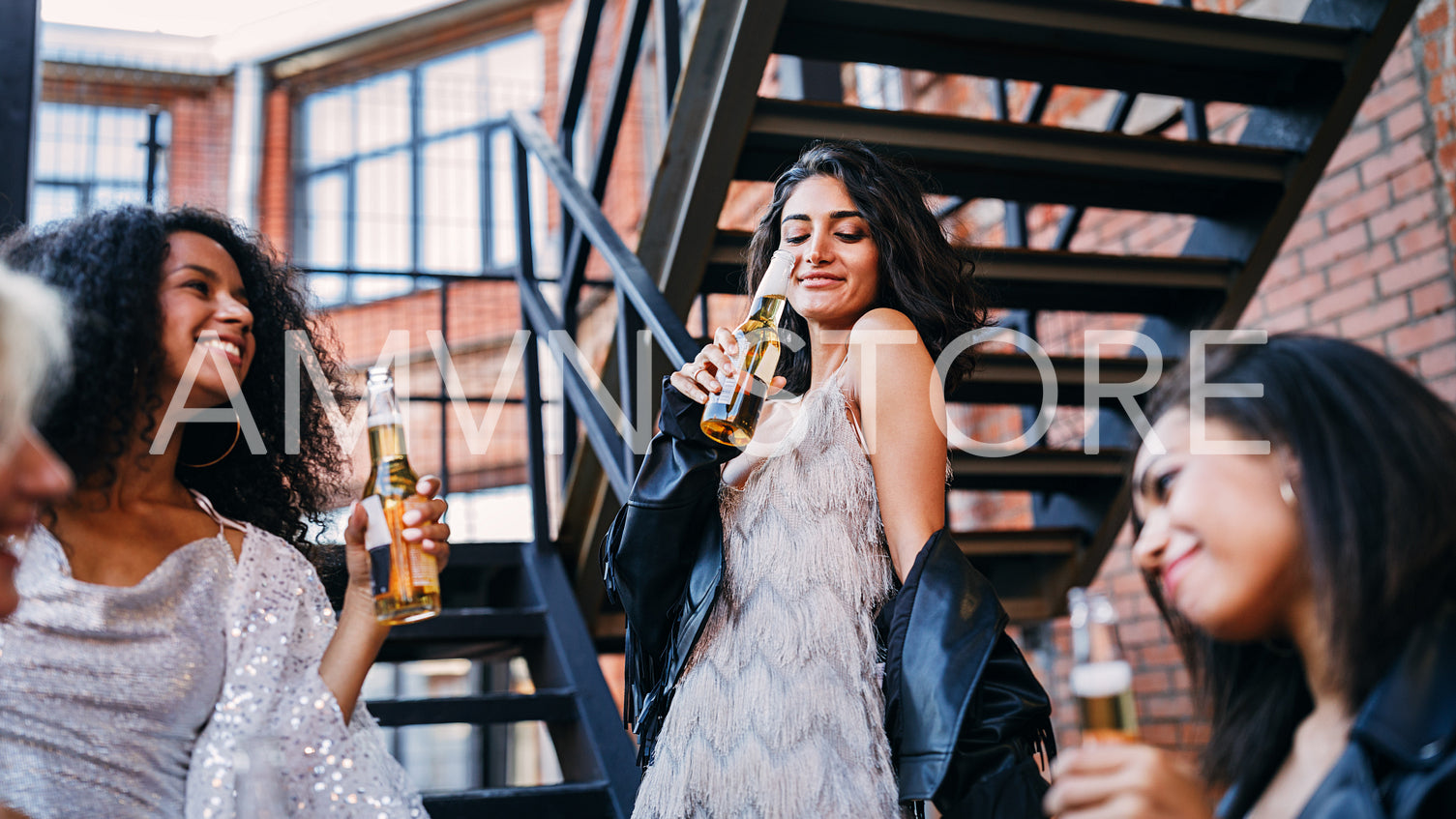 Young woman drinking beer from bottle surrounding by friends outdoors	