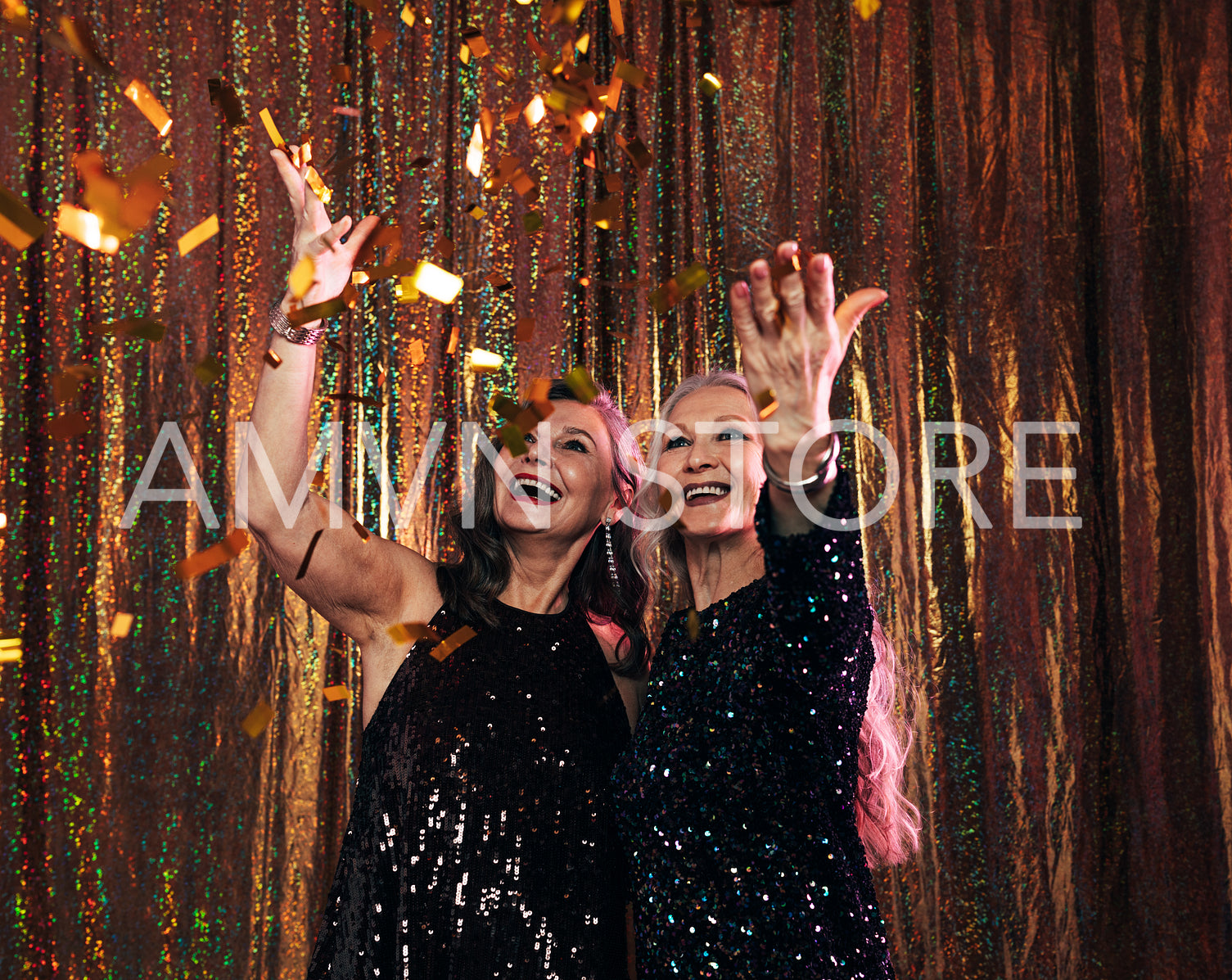 Two smiling senior women in black dresses throwing colorful conf