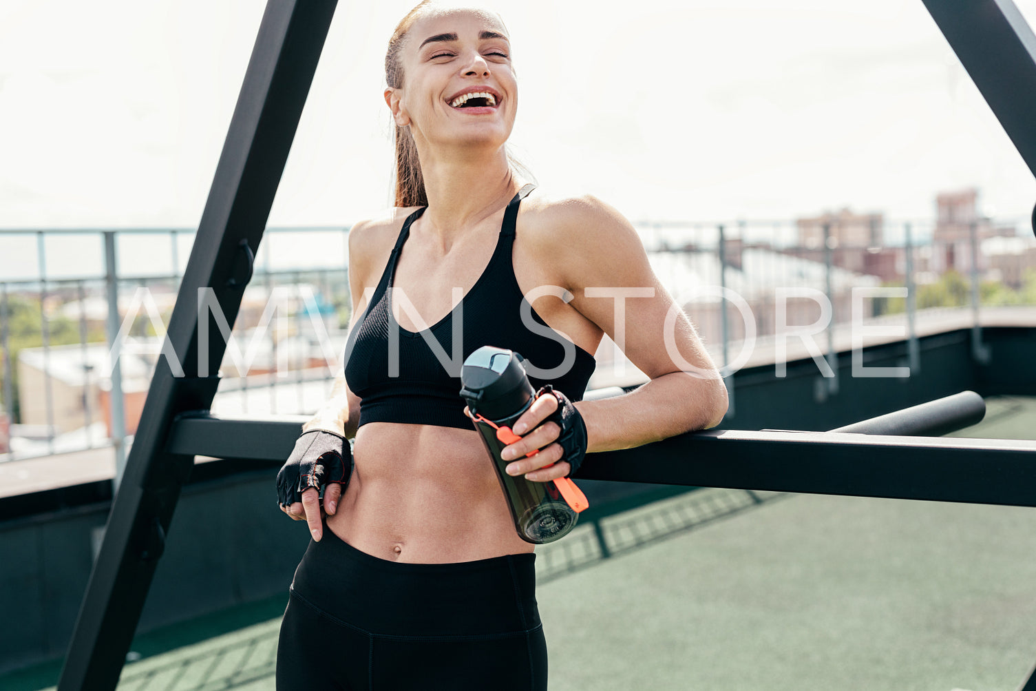 Happy woman holding a bottle. Fitness female standing on a terrace after training.	
