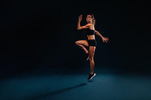 Female athlete jumping and stretching. Healthy woman exercising in studio warming up.