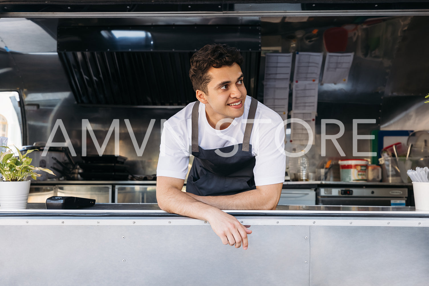 Young salesman in apron looking away from food truck window