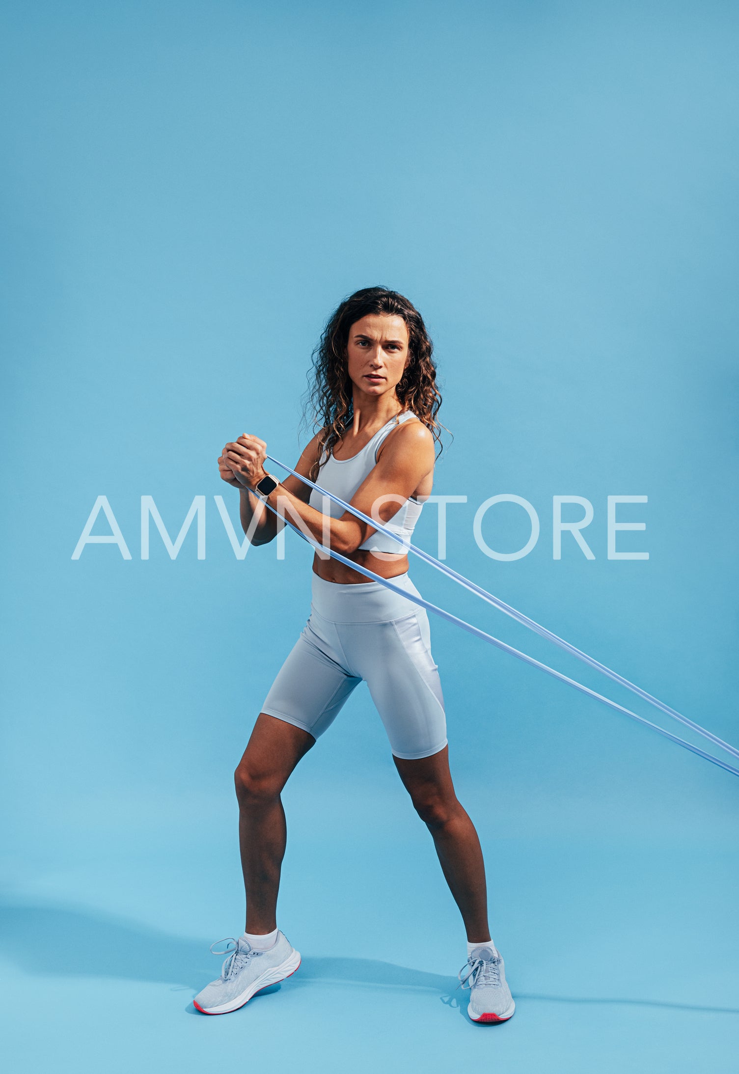 Slim muscular woman exercising with stretching band over blue background