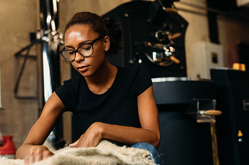 Young woman inspecting fresh coffee, sintting at sack in cafe