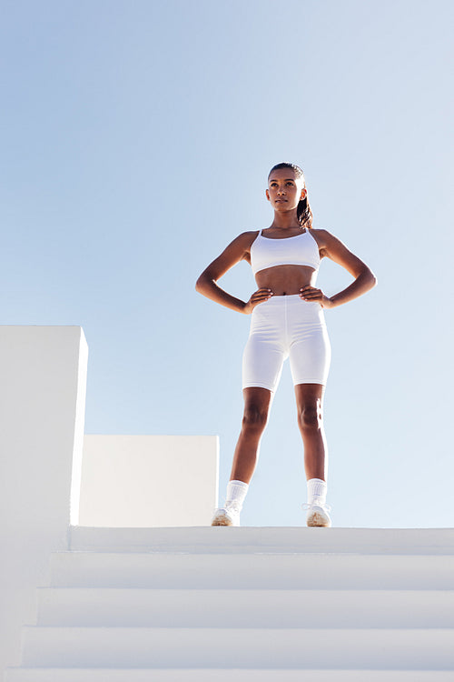 Full length of young slim sportswoman relaxing. Woman with hands on hips standing on the top of stairs.