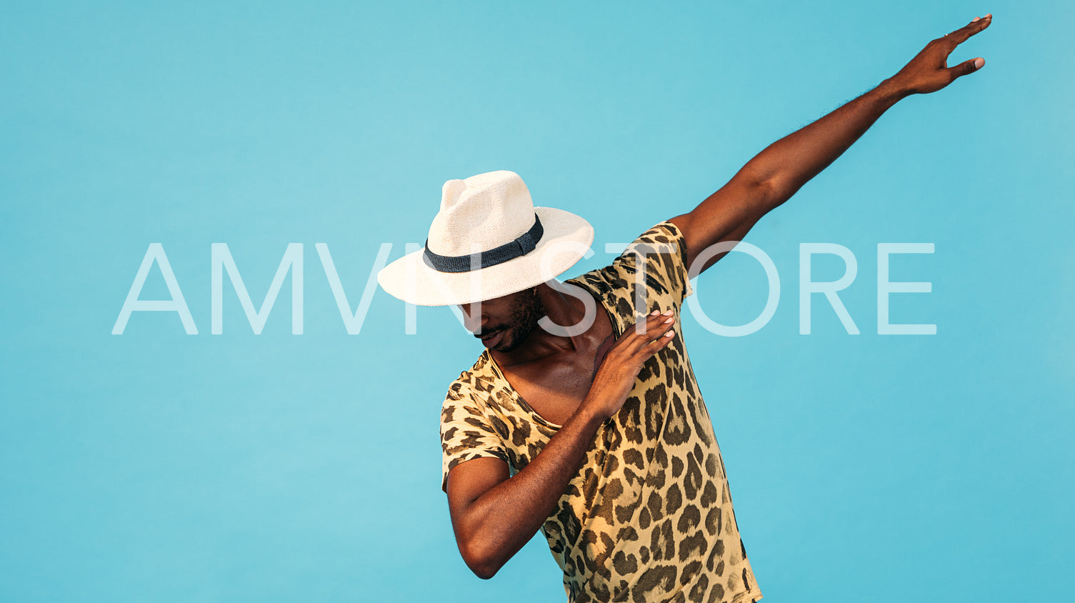 Young stylish guy in straw hat dancing in studio over blue background