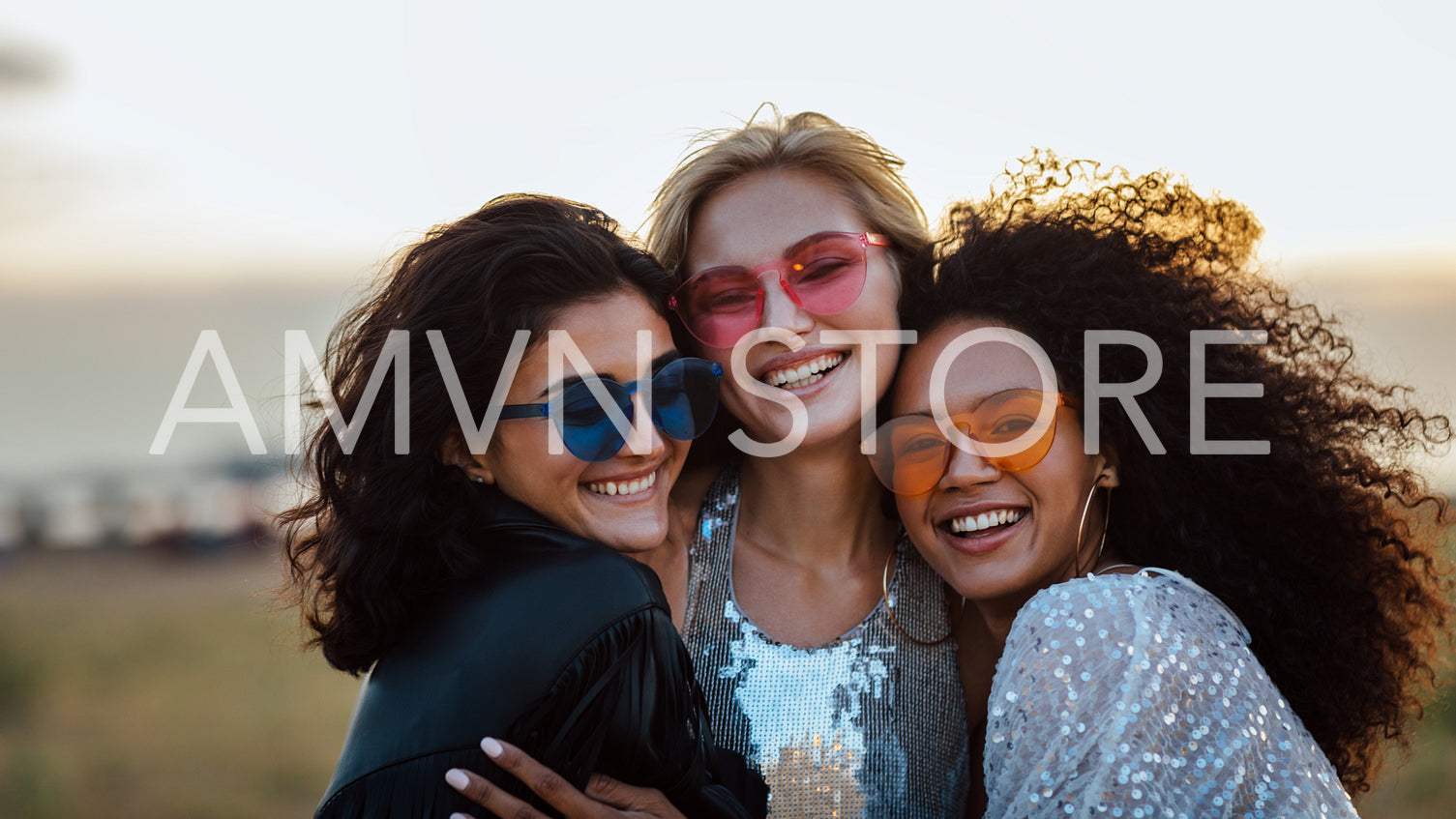 Three happy women wearing sunglasses hugging at evening outdoors	