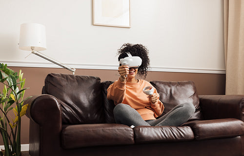 Woman in casual clothes relaxing at home. Mixed race female having fun while playing video games with VR set.