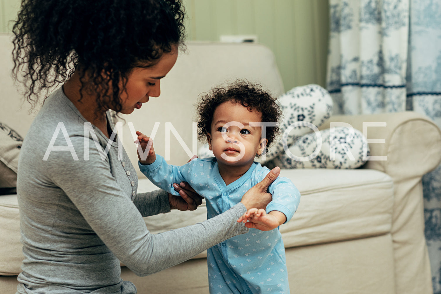 Mother sitting on the floor in room and teaching her baby son to walk	