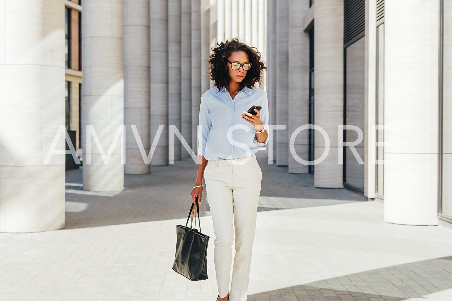 Businesswoman looking at smartphone while walking at modern office building	