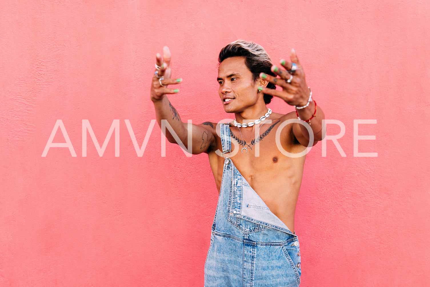 Young man wearing denim overall dancing while standing against pink wall