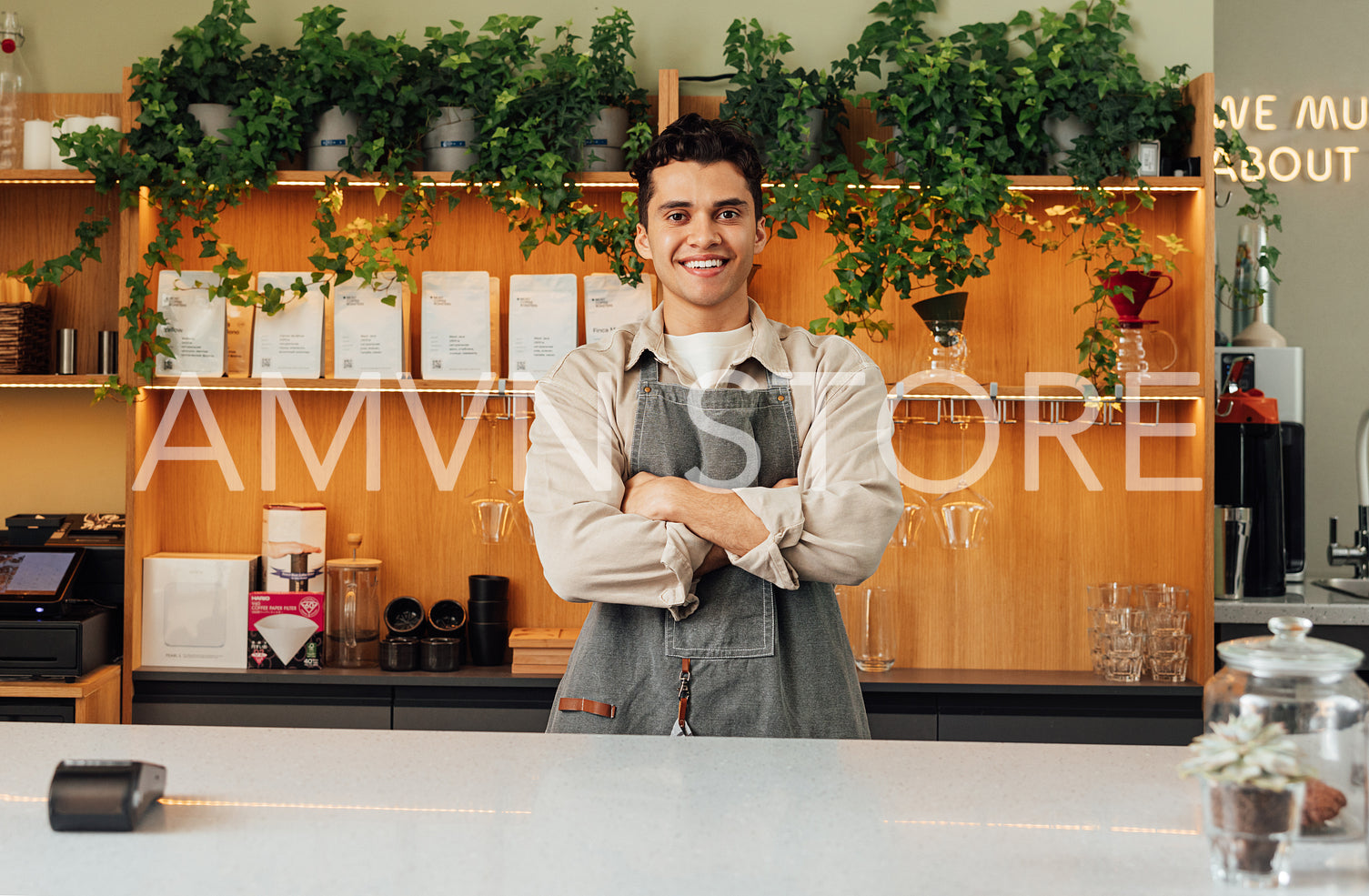 Confident male barista in an apron at the counter. Bartender with crossed hands looking at the camera and smiling.