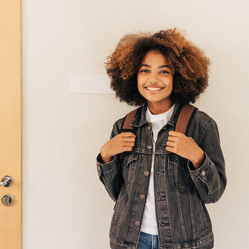 Beautiful teenager with curly hair wearing backpack and casual clothes while standing in college