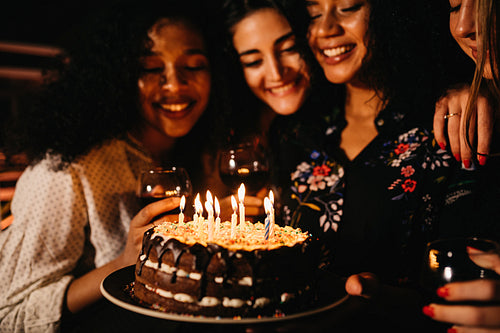 Young woman holding a birthday cake, making wish while friends look on