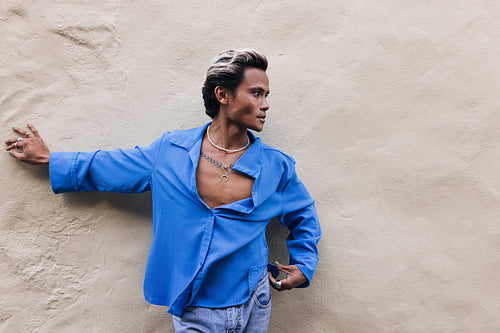 Side view of a young guy in a blue shirt leaning on a wall and looking away