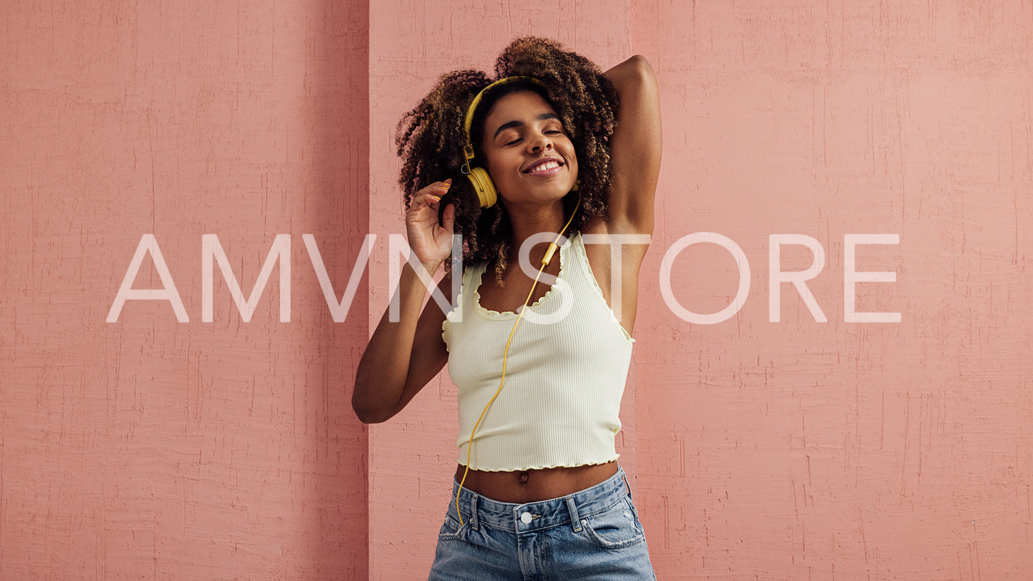 Beautiful woman with curly hair enjoying music with closed eyes against pink wall