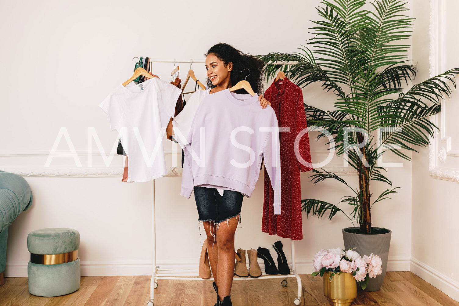 Young personal shopper holding hangers with clothes in studio	