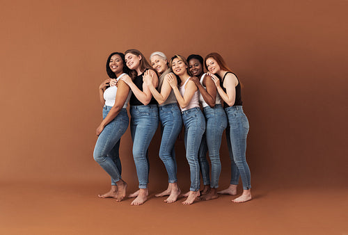 Full length of six smiling women embracing in studio. Females of different ages and body types posing over brown background.