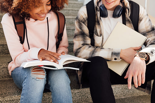 Cropped shot of two classmates sitting on stairs preparing assignments and smiling