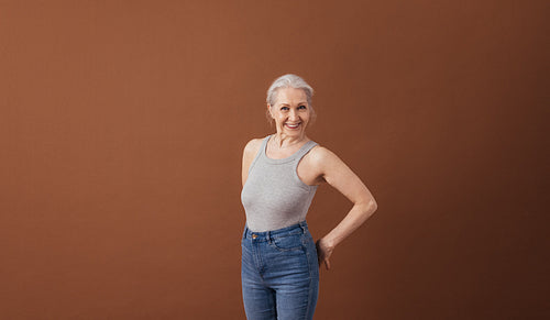 Portrait of a mature woman in casuals standing at brown background in studio